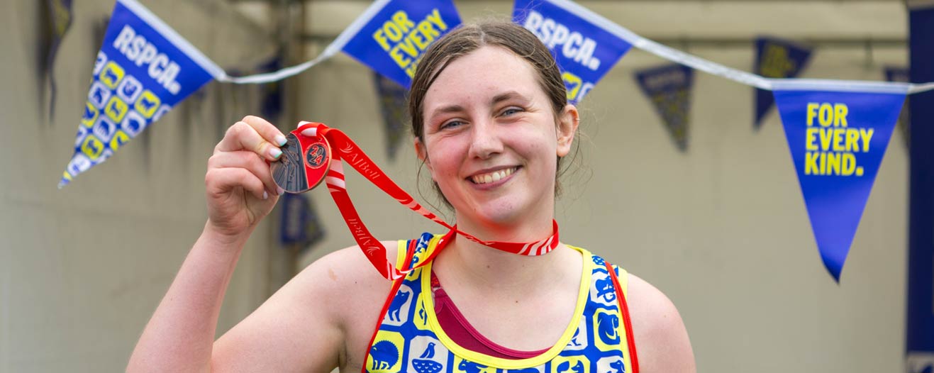 A young female runner smiling and holding up her finisher medal against RSCPA themed bunting.