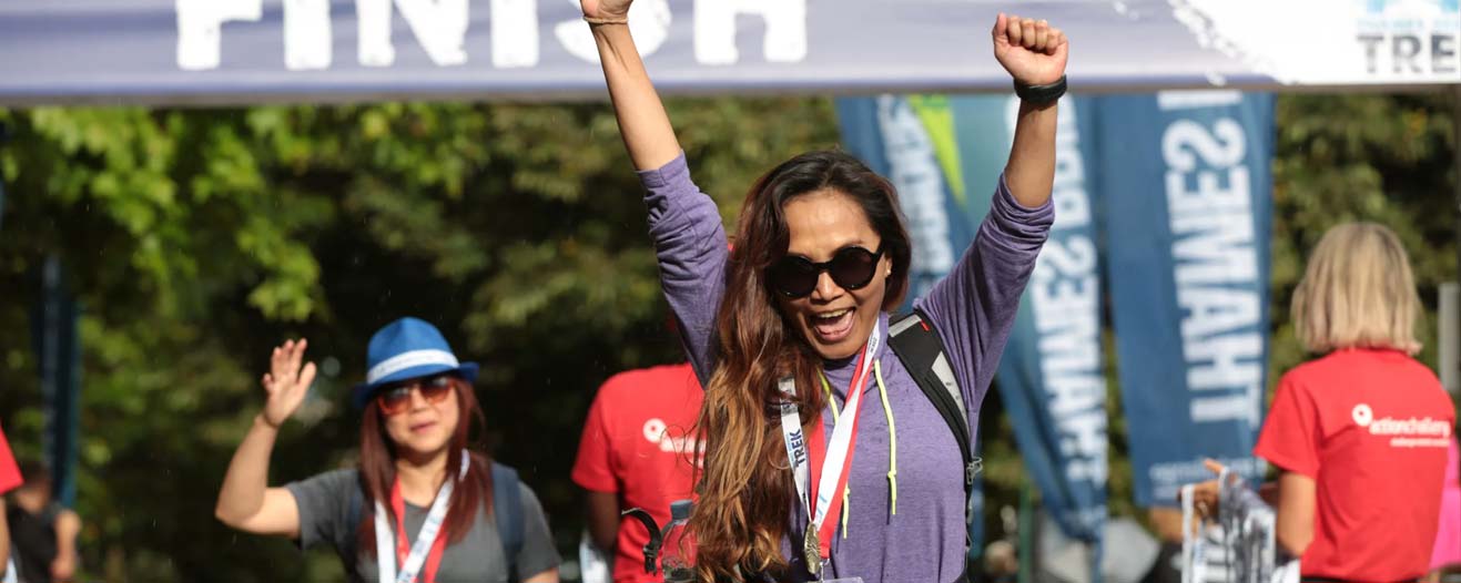 A happy female trekker with hands in the air at the finish line of the Thames Bridges Trek.