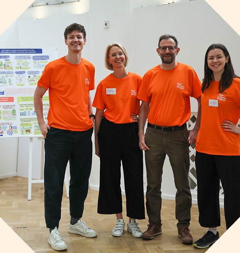 Four people wearing bright orange t-shirts standing in front of a large chart with colourful diagrams on it.