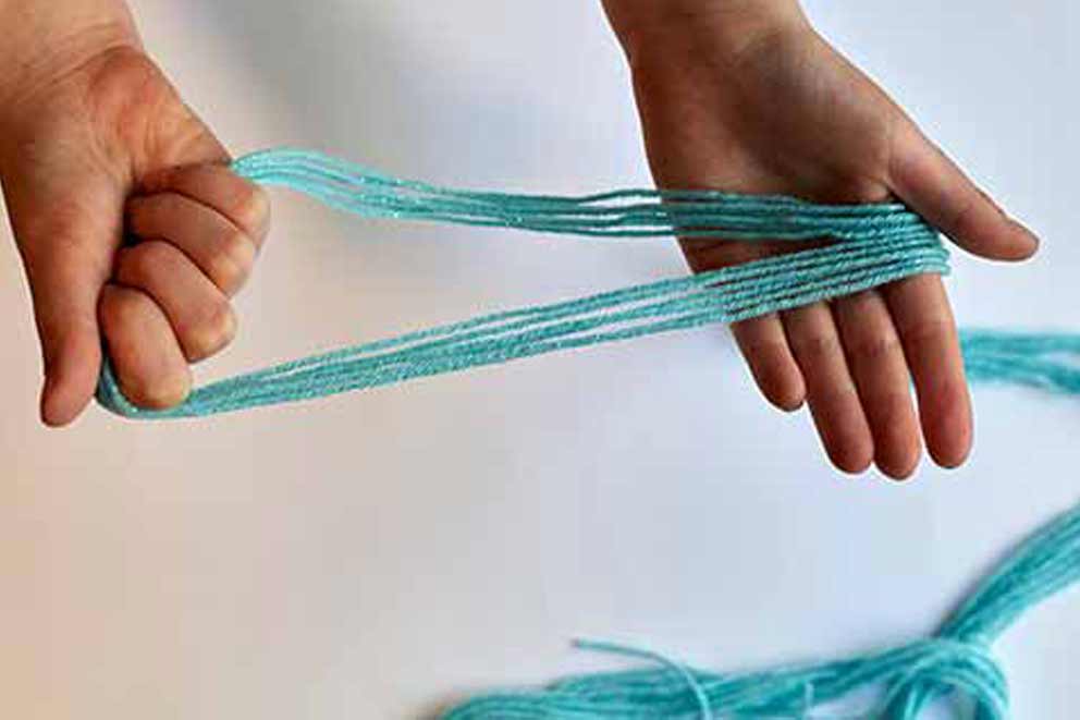Close-up of hands holding six folded strands of turquoise string to begin assembling a butterfly feeder hanger.