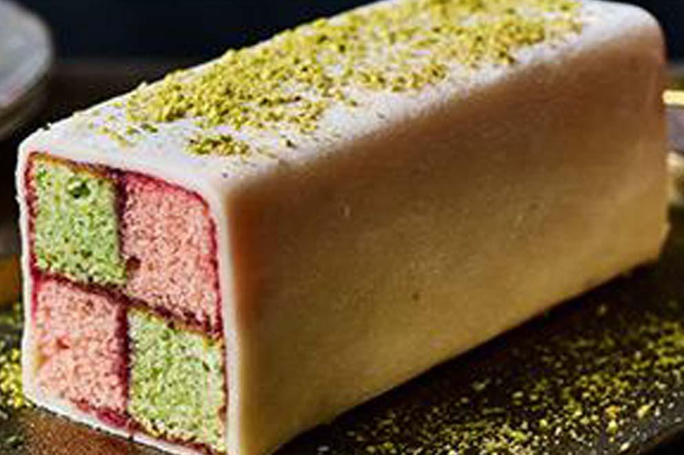 A freshly baked battenburg cake ready to be sliced with crumbled pistachio over the top.