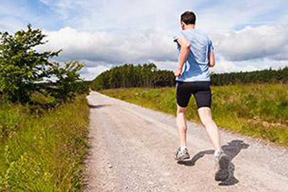 A single runner running on a concrete path in the countryside.