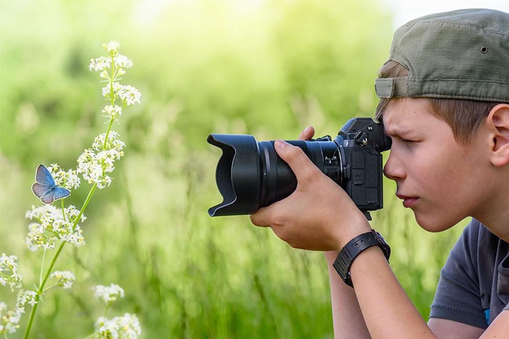 A young person setting up their camera to take a close-up of a butterfly resting on a flower.